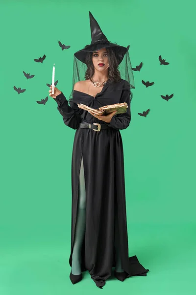 Young witch with spell book, candle and bats on green background