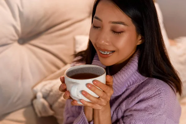 Young Asian woman with cup of coffee at home in evening, closeup