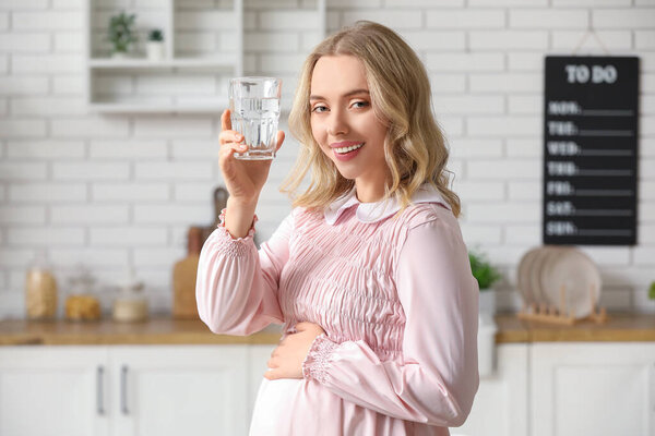 Young pregnant woman with glass of water in kitchen