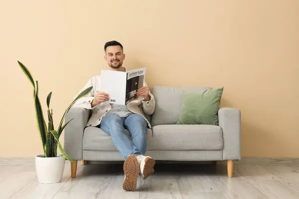 Handsome man reading magazine on sofa near beige wall