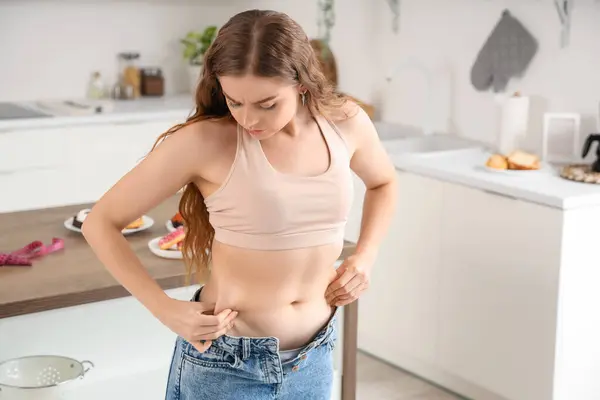 Young woman in tight jeans at home. Weight gain concept