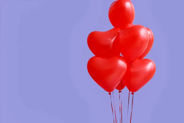 Red heart-shaped balloons for Valentine\'s Day celebration on lilac background, closeup