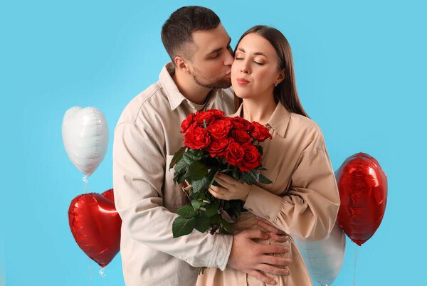 Lovely couple with bouquet of roses and heart-shaped balloons on blue background. Valentine's Day celebration