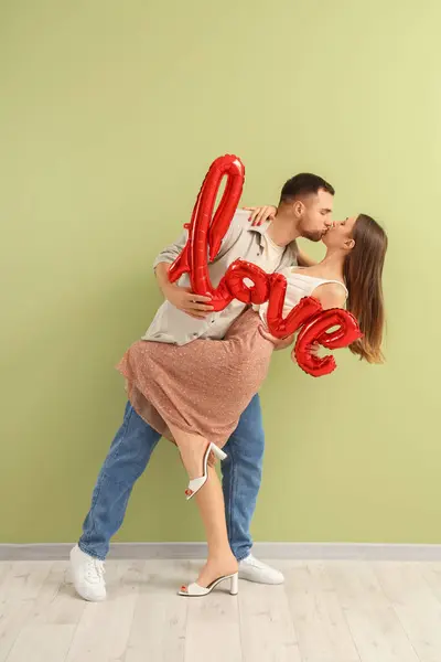 Lovely couple with word LOVE made from balloons on green background. Valentine's Day celebration