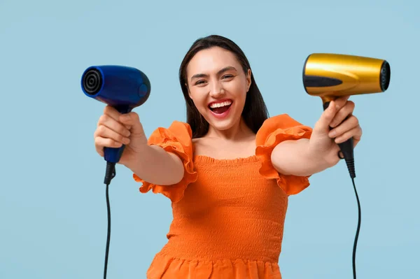 Beautiful young woman with hair dryers  on light blue background