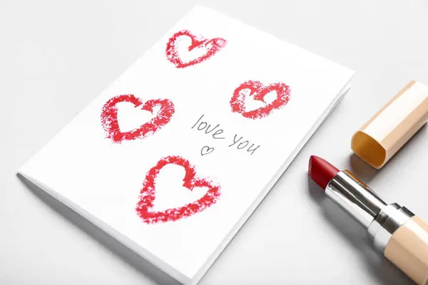 Greeting card with text LOVE YOU and red lipstick on grey background, closeup. Valentine\'s Day celebration