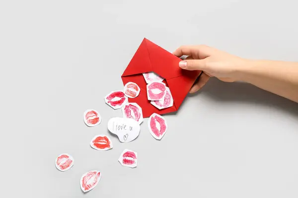 Female hand with red envelope, paper lipstick kiss marks and text I LOVE U on grey background, closeup. Valentine\'s Day celebration