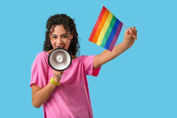 Young African-American woman with rainbow flag and megaphone on blue background. LGBT concept