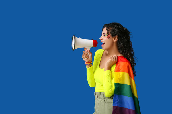 Young African-American woman with rainbow flag and megaphone on blue background. LGBT concept