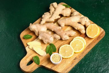 Taze zencefil köklü ahşap tahta, dilimlenmiş limon ve yeşil arka planda bir kase kuru toz.