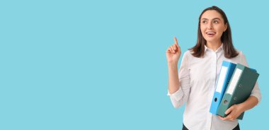 Mavi arkaplanda metin için yeri olan bir şeye işaret eden belge klasörleri olan genç iş kadını