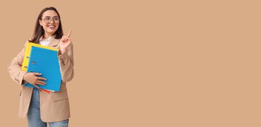 Belge klasörleri olan genç iş kadını bej arkaplan ve metin için yeri olan bir şeyi işaret ediyor