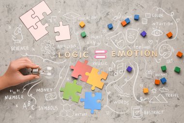 Hand with light bulb, words LOGIC, EMOTION, cubes and puzzle pieces on grunge background