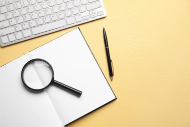 Blank open book, magnifier, keyboard and pen on yellow background. World Poetry Day celebration