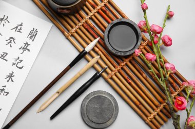 Kaligrafi malzemeleriyle kompozisyon ve arka planda çiçek açan bir dal, yakın plan. Uluslararası Haiku Şiir Günü