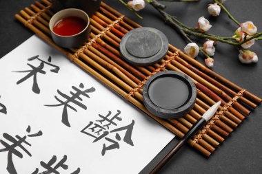 Asyalı hiyeroglifler, fırça, mürekkep, bir fincan çay ve koyu arkaplanda çiçek açan bir dal, yakın plan. Uluslararası Haiku Şiir Günü