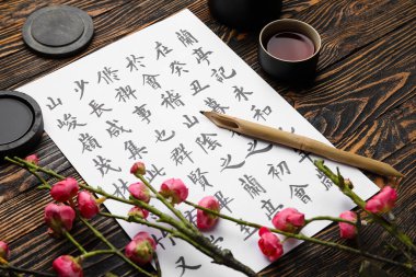 Kağıt çarşaf, Asya hiyeroglifleri, kalem, mürekkep, çay fincanı ve tahta arka planda çiçek açan dal, yakın plan. Uluslararası Haiku Şiir Günü
