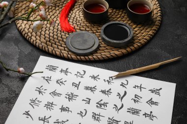 Asya hiyeroglifleri, mürekkep, uçlu kalem ve koyu arka planda bir fincan çay, yakın plan. Uluslararası Haiku Şiir Günü
