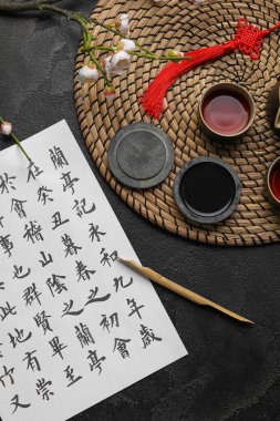 Üzerinde Asya hiyeroglifleri, mürekkep, uçlu kalem ve koyu arkaplanda bir fincan çay olan kağıt çarşaf. Uluslararası Haiku Şiir Günü