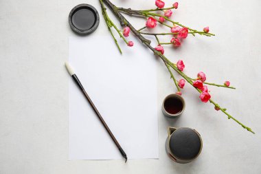 Açık arkaplanda boş kağıt, mürekkep, fırça ve çiçek açan dalla kompozisyon. Uluslararası Haiku Şiir Günü