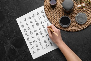 Koyu arkaplana Asya hiyeroglifleri yazan bir kadın. Uluslararası Haiku Şiir Günü