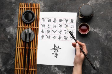 Asyalı hiyeroglifleri, fırçaları ve grunge arka planda bir fincan çayı olan kadın eli. Uluslararası Haiku Şiir Günü