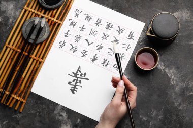 Asya hiyeroglifleri, fırçalar ve arka planda bir fincan çay olan kadın eli, yakın plan. Uluslararası Haiku Şiir Günü