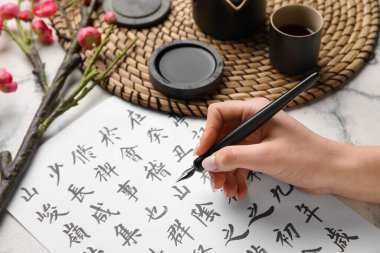 Hafif arkaplana Asya hiyeroglifleri yazan kadın, yakın plan. Uluslararası Haiku Şiir Günü