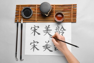 Hafif arkaplanda Asya hiyeroglifleri, fırçalar, mürekkep ve bir fincan çay olan kadın eli. Uluslararası Haiku Şiir Günü