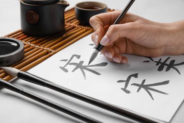 Hafif arkaplana Asya hiyeroglifleri yazan kadın, yakın plan. Uluslararası Haiku Şiir Günü