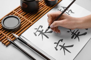 Hafif arkaplana Asya hiyeroglifleri yazan kadın, yakın plan. Uluslararası Haiku Şiir Günü