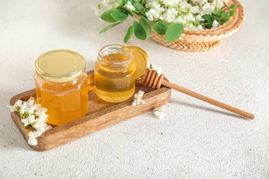 Arkaplanda akasya çiçekleri olan bal kavanozları, yakın plan.