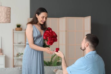 Genç adam evde çiçeklerle kız arkadaşına evlenme teklif ediyor.