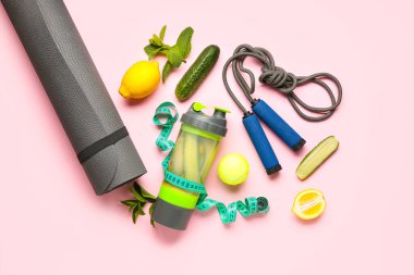 Bir şişe salatalıklı limonata ve pembe arka planda spor malzemeleri.