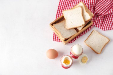 Haşlanmış tavuk yumurtası ve beyaz arka planda ahşap ekmek kutusu olan tutucular.