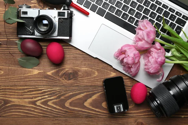 Photographer\'s equipment with laptop, Easter eggs and flowers on wooden background