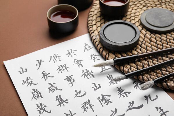 Бумажный лист с азиатскими иероглифами, кисточками, чернилами и чашками чая на цветном фоне, крупным планом. Международный день поэзии Хайку
