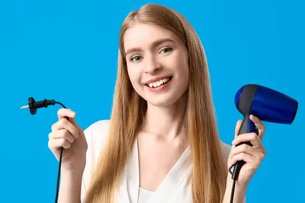 Young blonde woman with hair dryer on blue background, closeup