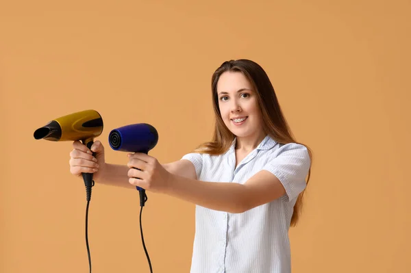 Beautiful young woman with hair dryers on beige background