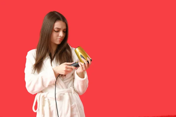 Displeased young woman with hair dryer on red background