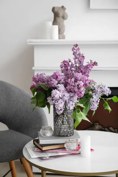 Vase with lilac flowers, books and candles on table in living room