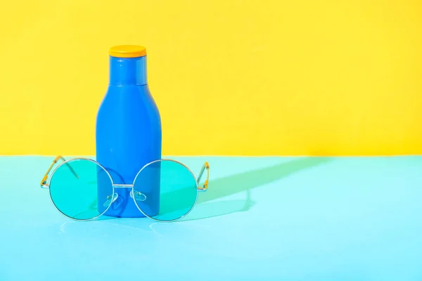 Bottle of sunscreen cream with sunglasses on blue table near yellow wall