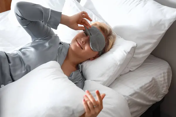 Young woman with sleeping mask waking up in bed