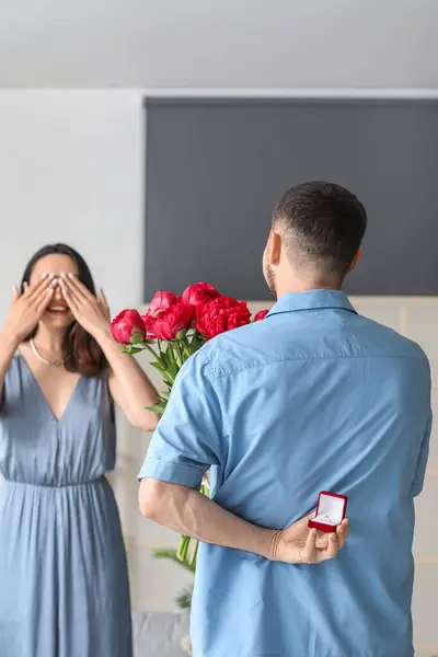 Young man with flowers proposing to his girlfriend at home, back view