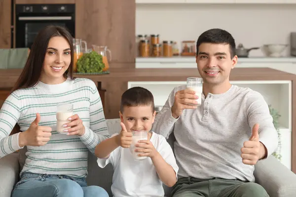 Happy family with glasses of milk showing thumbs-up at home