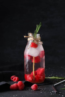 Siyah arka planda biberiyeli bir şişe taze ahududu limonatası.