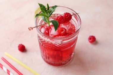 Bir bardak taze ahududu limonatası, pembe arka planda naneli.