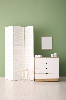 Katlanan ekran, çekmeceler ve yeşil duvarın yanındaki tabure.