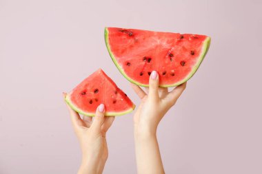 Bej arkaplanda olgun karpuz parçaları olan kadın elleri.