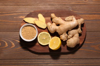 Tahta zemin üzerinde taze zencefil kökleri, limon ve bir kase kurutulmuş toz olan tahta.